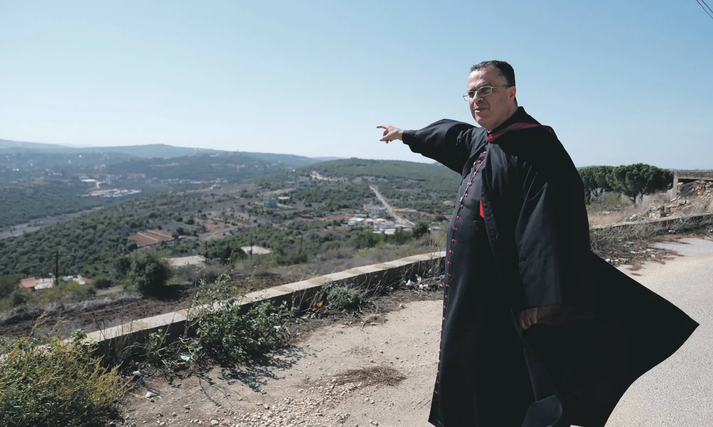 L’archevêque maronite de Tyr, Monseigneur Abdallah, montre la frontière avec Israël, située au sommet de la colline visible au loin. ©Gaby Leygues
