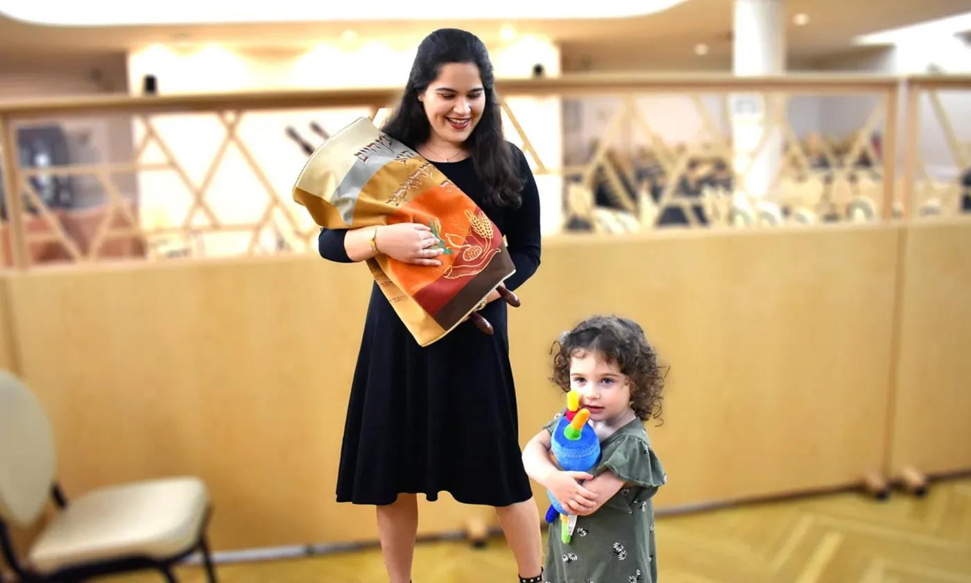 Une femme juive orthodoxe tient un rouleau de la Torah tandis que sa fille embrasse un jouet de la Torah. RNS