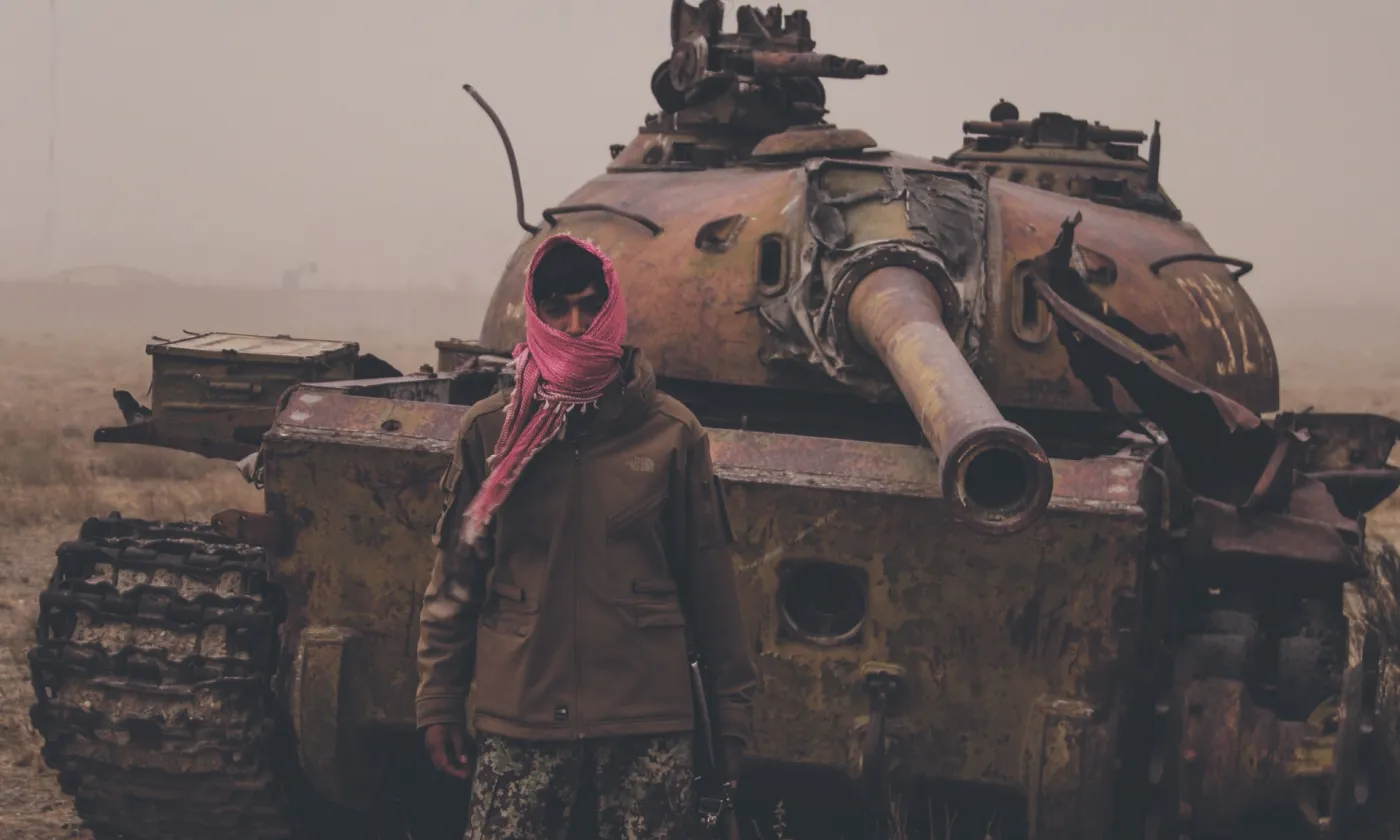 Août 2021, dans un faubourg de Kaboul (Afghanistan), un homme armé pose devant une épave de tank taliban. ©iStock/Trent Inness